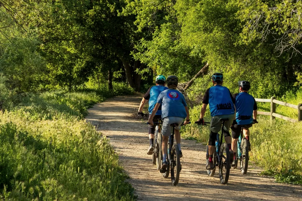 Grupa rowerzystów na polnej drodze wzdłuż płotu